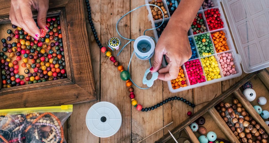 Surrounded by a plethora of colorful beads, a hand is crafting a necklace.